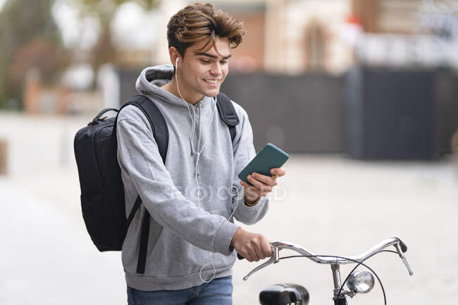 Улыбающийся молодой человек, использующий мобильный телефон во время езды на велосипеде по городу — стоковое фото