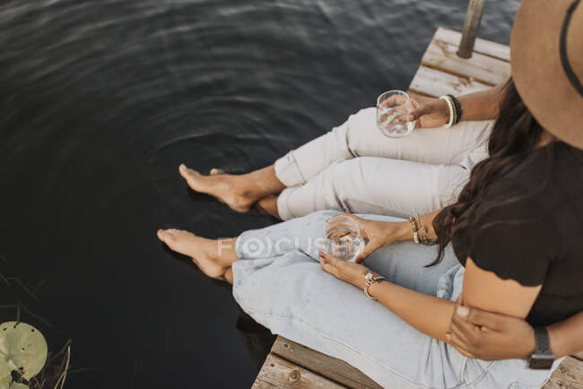 Fidanzato e fidanzata bere vino mentre seduto sul molo — Foto stock