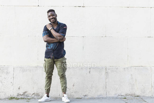 Улыбающийся молодой человек в повседневной жизни, стоящий напротив белой стены — стоковое фото