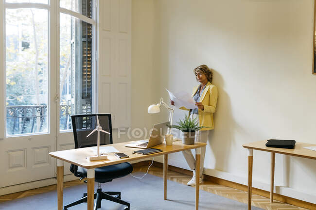 Empresaria examinando plano mientras está de pie contra la pared en la oficina - foto de stock