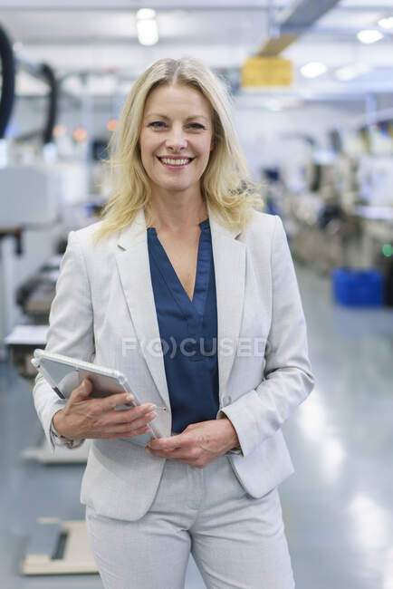 Lächelnde blonde Geschäftsfrau hält digitales Tablet in der Hand, während sie in der beleuchteten Industrie steht — Stockfoto
