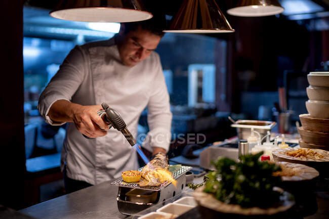 Male chef using blow torch while preparing seafood in kitchen at restaurant — Stock Photo