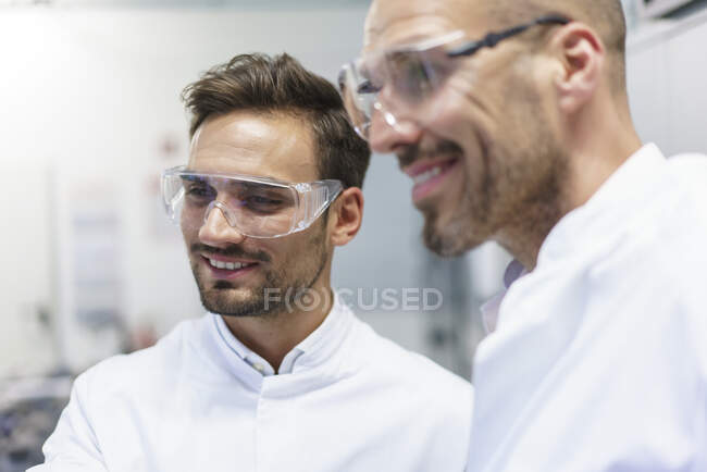 Smiling male technicians looking away at illuminated laboratory — Stock Photo