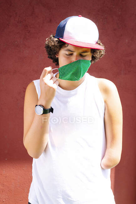 Teenage boy wearing face mask while standing against wall on sunny day — Stock Photo