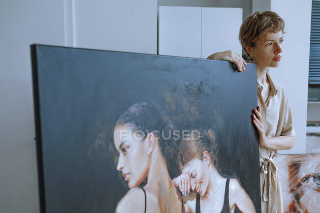 Thoughtful female artist standing by painting in art studio — Stock Photo