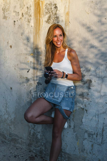 Lächelnde erwachsene Frau mit Handy an Wand gelehnt — Stockfoto