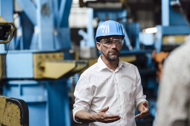 Businessman wearing protective eyewear discussing with unrecognizable person at industry — Stock Photo