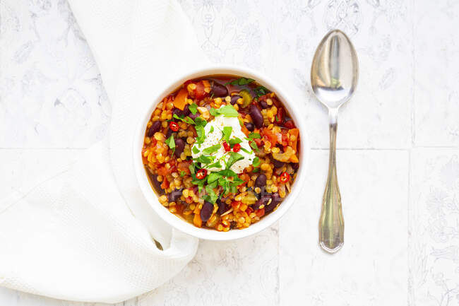Schüssel vegetarischer Eintopf mit roten Linsen, Chilischoten, Sellerie, Nierenbohnen, Tomaten, Karotten und saurer Sahne — Stockfoto
