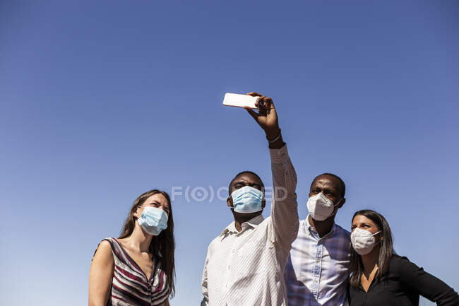 Professionnels des affaires prenant selfie avec des masques protecteurs contre le ciel bleu clair par une journée ensoleillée — Photo de stock