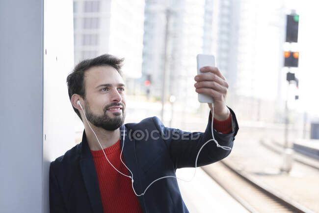 Empreendedor sorridente com fones de ouvido na parede na plataforma ferroviária — Fotografia de Stock