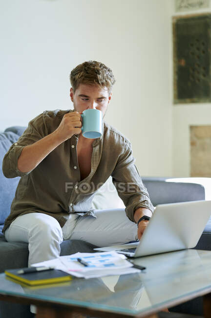 Homme d'affaires boire du café tout en travaillant sur un ordinateur portable à la maison — Photo de stock