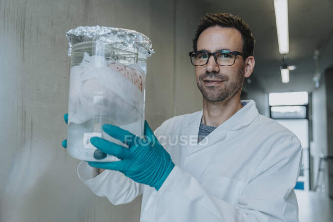 Científico sosteniendo vaso de precipitados preservado cerebro humano mientras está de pie en el corredor de la clínica - foto de stock