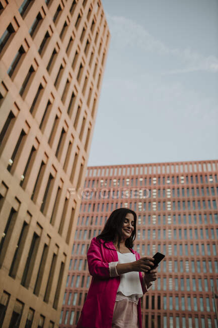 Messaggistica di testo femminile imprenditore su smartphone mentre in piedi contro gli edifici — Foto stock
