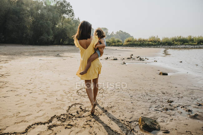 Mère portant fille tout en marchant sur le sable à la plage — Photo de stock