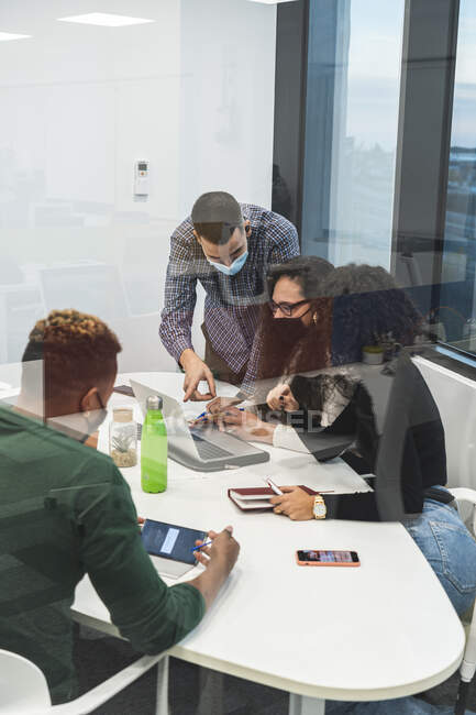 Empresario y empresaria discutiendo sobre portátil en reunión en la oficina durante COVID-19 - foto de stock