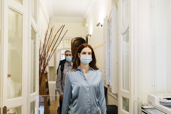 Businesswoman in protective face mask walking with coworkers in corridor — Stock Photo