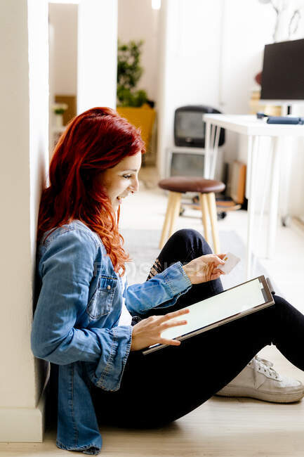 Рыжая деловая женщина делает покупки в Интернете через цифровой планшет, сидя в офисе — стоковое фото