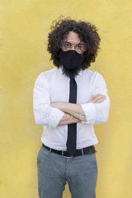 Geschäftsmann mit Mundschutz und Brille steht mit verschränkten Armen an der Wand — Stockfoto