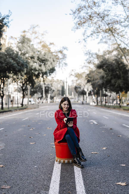 Young woman in red jacket using digital tablet while sitting on chair at road — Stock Photo