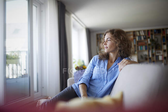 Woman looking at window while sitting on sofa at home — Stock Photo