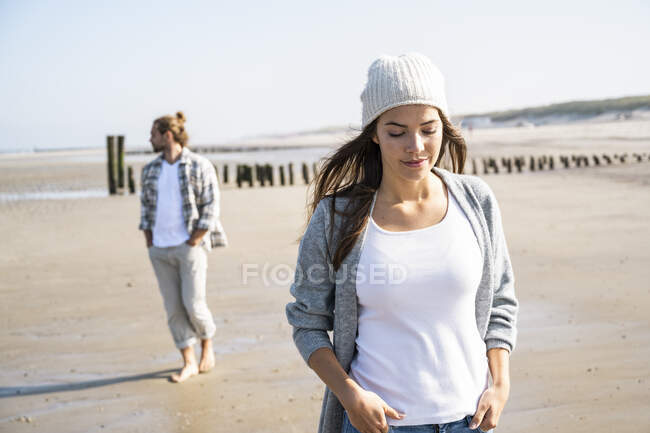 Задумчивая женщина с руками в карманах на пляже в солнечный день — стоковое фото