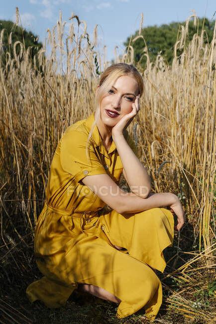 Bella donna bionda accovacciata contro i raccolti in campo nella giornata di sole — Foto stock