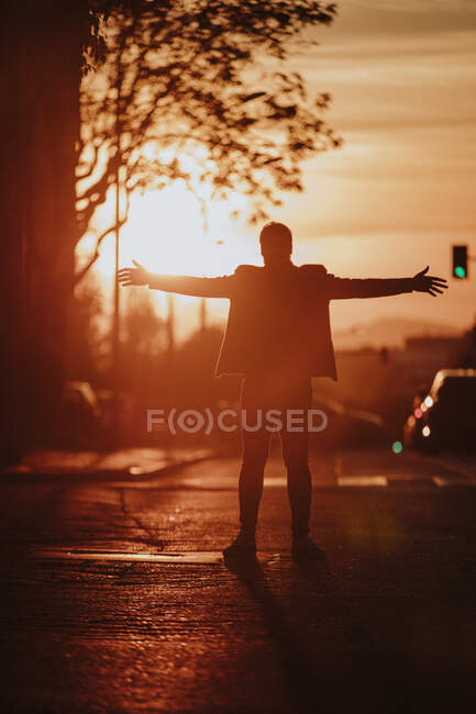Silhouette eines Mannes, der bei Sonnenuntergang mit ausgestreckten Armen auf der Straße steht — Stockfoto