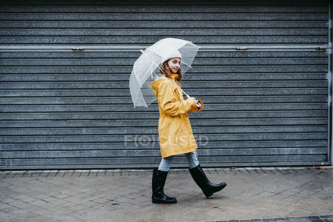 Girl wearing raincoat and jump boot walking on sidewalk outdoors — Stock Photo