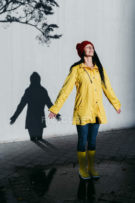 Жінка в плащі стоїть на дощу калюжі до стіни тіней. — стокове фото