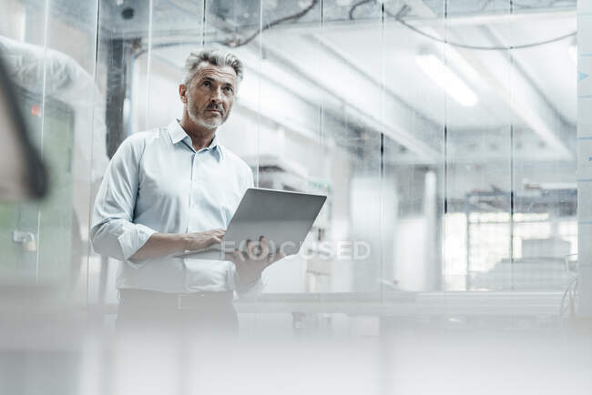 Contemplating male engineer with laptop looking away while standing in industry — Stock Photo