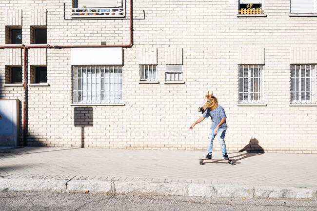 Uomo indossando maschera cavallo mentre skateboard sul sentiero contro edificio in città durante la giornata di sole — Foto stock