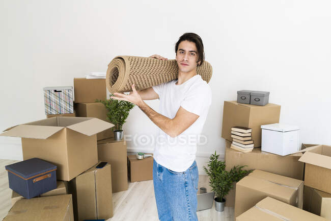 Giovane uomo che trasporta tappeto sulla spalla mentre si trasferisce in una nuova casa — Foto stock