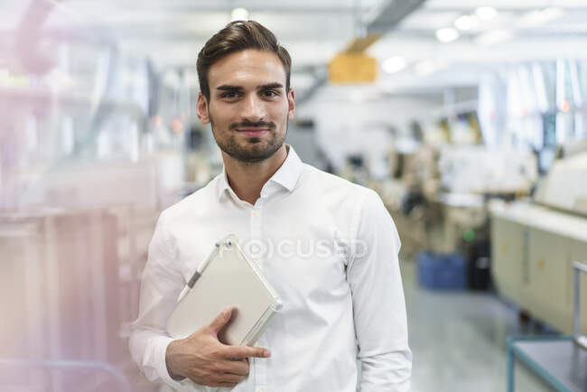 Впевнений молодий чоловічий інженер, який тримає цифрову табличку, стоячи на освітленій фабриці. — стокове фото