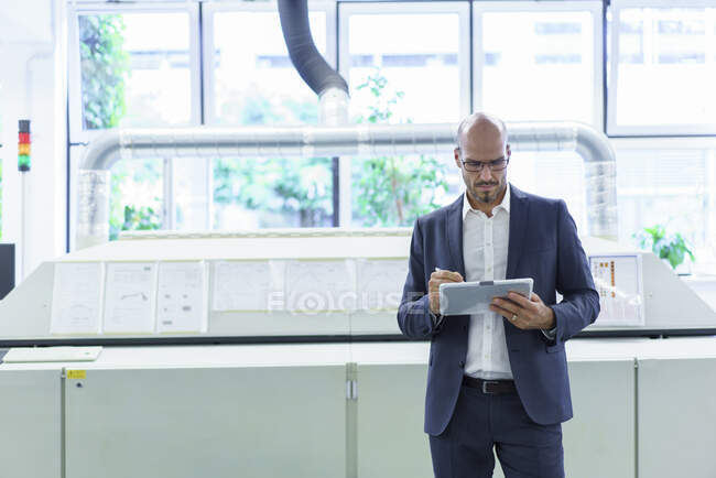 Homem de negócios careca usando tablet digital enquanto está de pé contra máquinas na fábrica — Fotografia de Stock