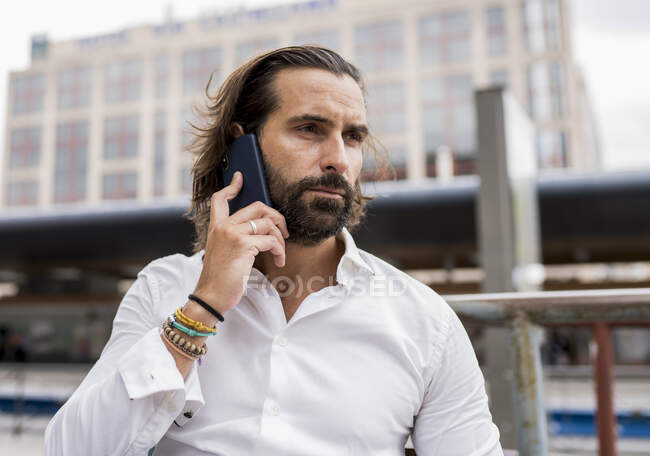 Retrato sincero de empresário barbudo sentado ao ar livre e falando no telefone inteligente — Fotografia de Stock