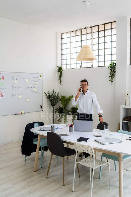 Businessman talking on smart phone while standing at desk in creative workplace — Stock Photo