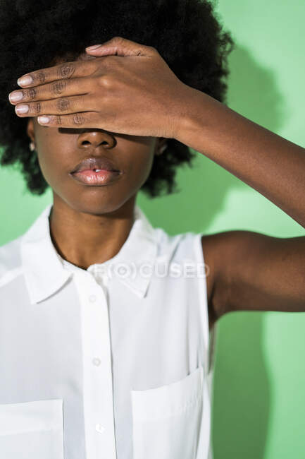 Mujer cubriendo los ojos con la mano mientras está de pie sobre fondo verde - foto de stock