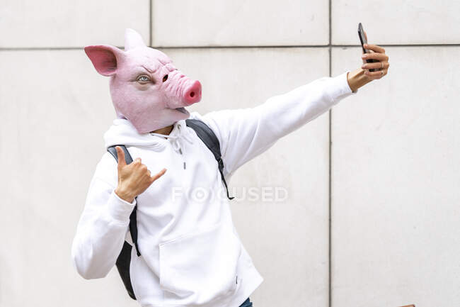 Man with pig mask taking selfie on smart phone against wall — Stock Photo