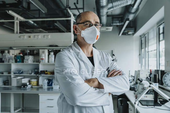 Selbstbewusster Wissenschaftler mit Mundschutz steht mit verschränkten Armen im Labor — Stockfoto