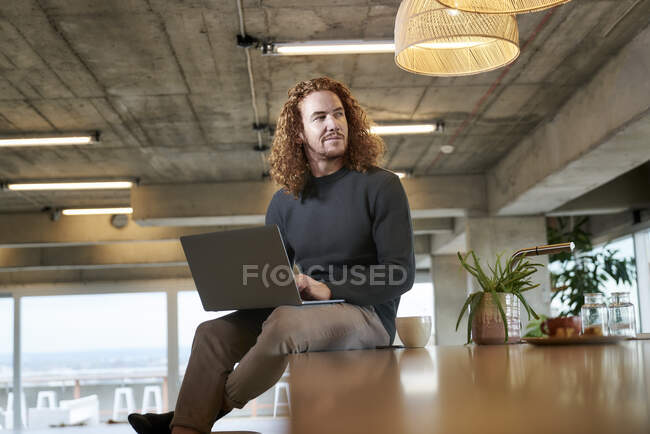 Ragionevole uomo rossa guardando lontano mentre si utilizza il computer portatile seduto a casa — Foto stock