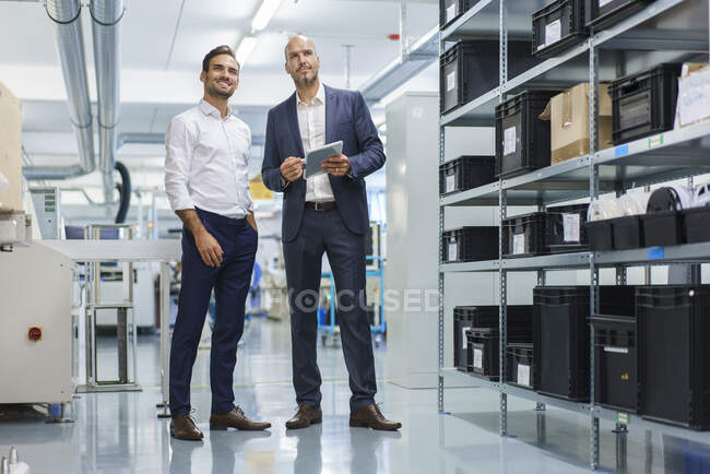 Бизнесмен, держащий цифровой планшет, стоя рядом с улыбающимся инженером и глядя в сторону фабрики — стоковое фото