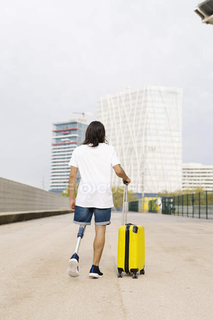 Disabled man walking with luggage at sidewalk in city — Stock Photo