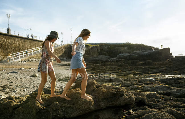 Jeunes femmes marchant sur les rochers à la plage contre le ciel — Photo de stock