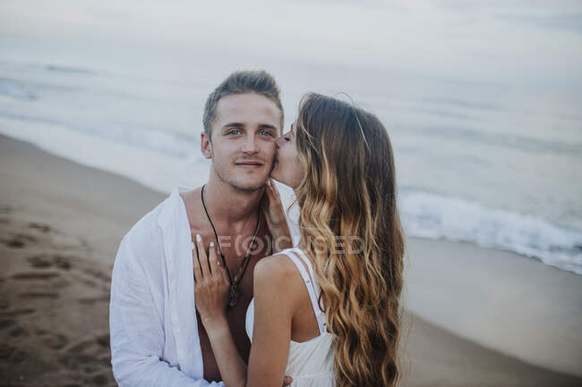 Giovane donna baciare uomo mentre in piedi in spiaggia — Foto stock