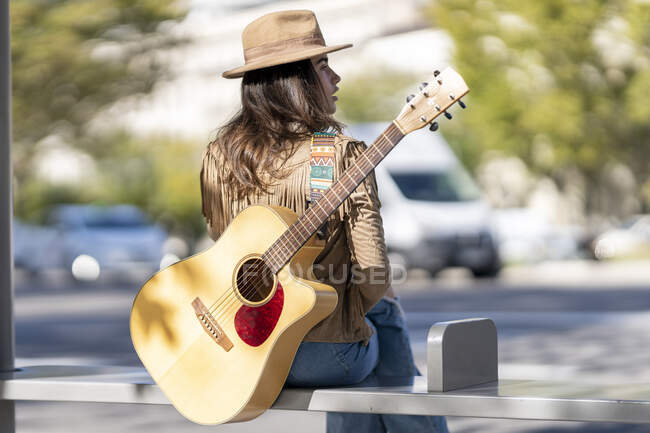 Mujer joven con guitarra sentada en la parada de autobús - foto de stock