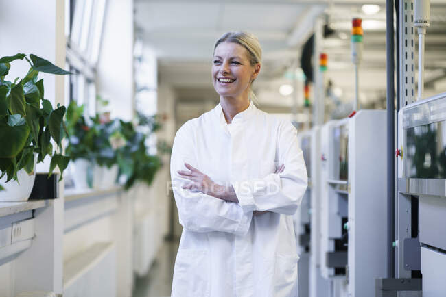 Cientista feminina madura confiante com as mãos em bolsos jaleco de pé por máquinas em laboratório — Fotografia de Stock