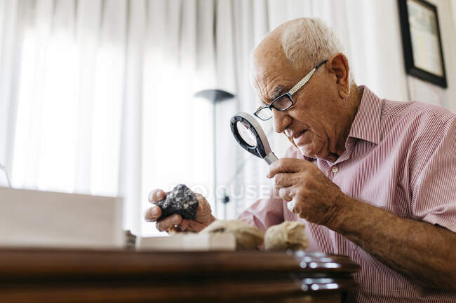 Rentner mit Lupe für die Erforschung von Fossilien und Mineralien zu Hause — Stockfoto