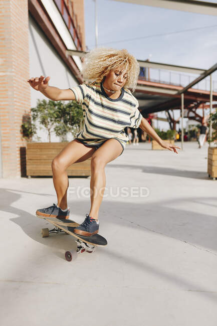 Blond woman with arms outstretched skateboarding on footpath during sunny day — Stock Photo