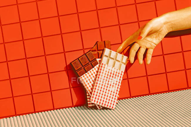 Mediados de la mano de la mujer adulta elegir chocolate mantenido en línea contra la pared de baldosas rojas - foto de stock