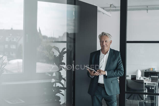Усміхаючись бізнесмен, стоячи при офісі, користується цифровою табличкою. — стокове фото